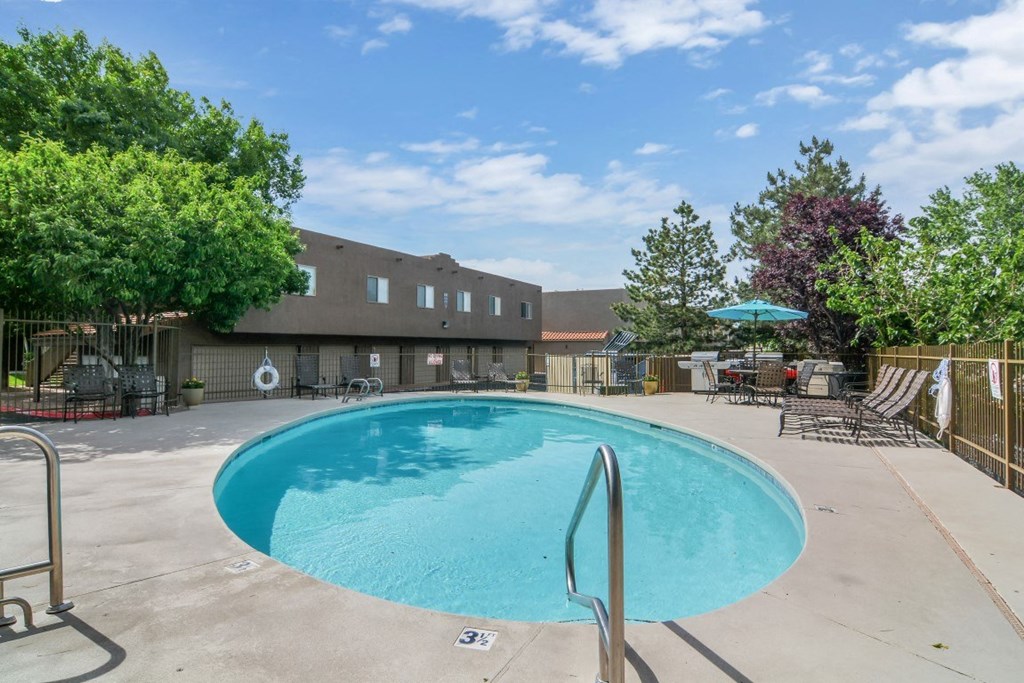 A large outdoor swimming pool surrounded by trees and a building in the background.